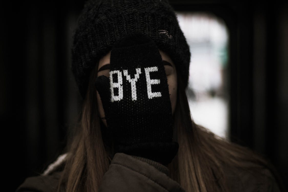 young woman holding glove over face with word "bye" stitched on it